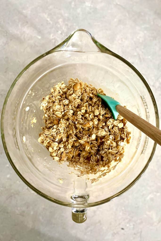 Oats, Nuts, and Peanut Butter Mixture in Mixing Bowl Being Stirred with Spatula.