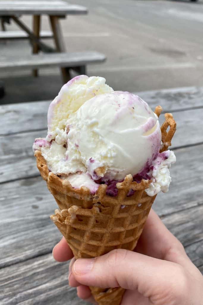 Scoop of blueberry lime cheesecake ice cream in a waffle cone.
