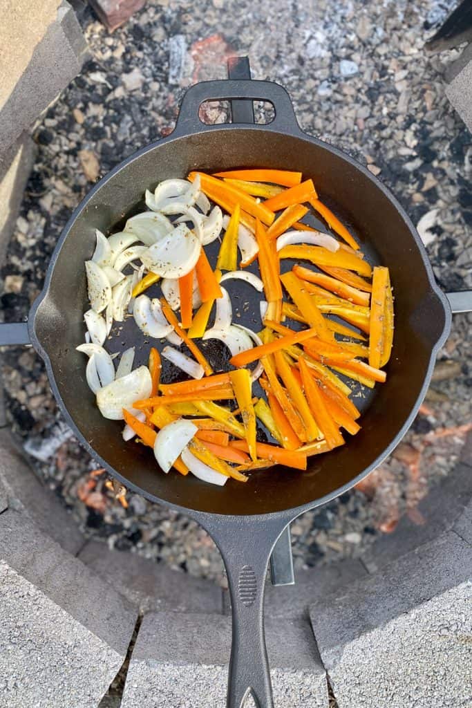 Vegetables tossed with seasoning and oil in cast-iron pan.
