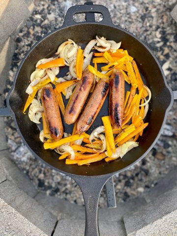 Cooked onions and peppers and sausages in cast-iron pan.