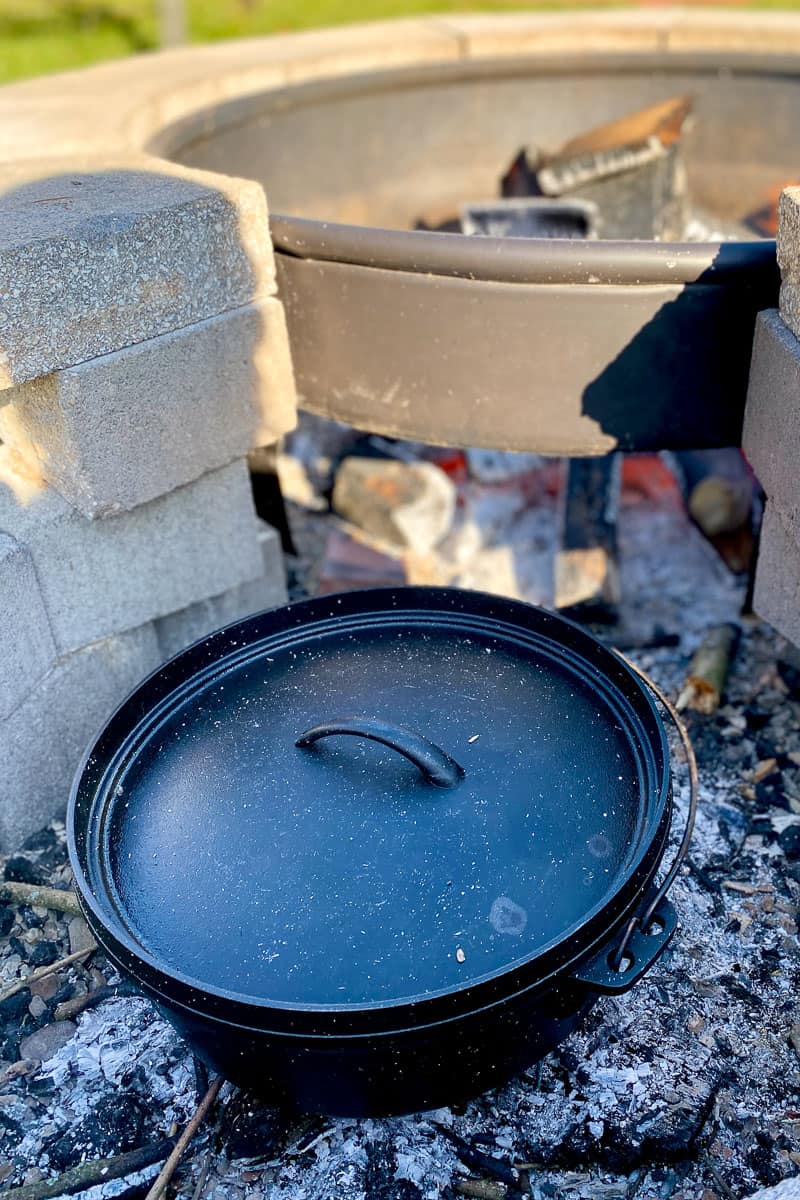 Dutch oven with lid on campfire coals.