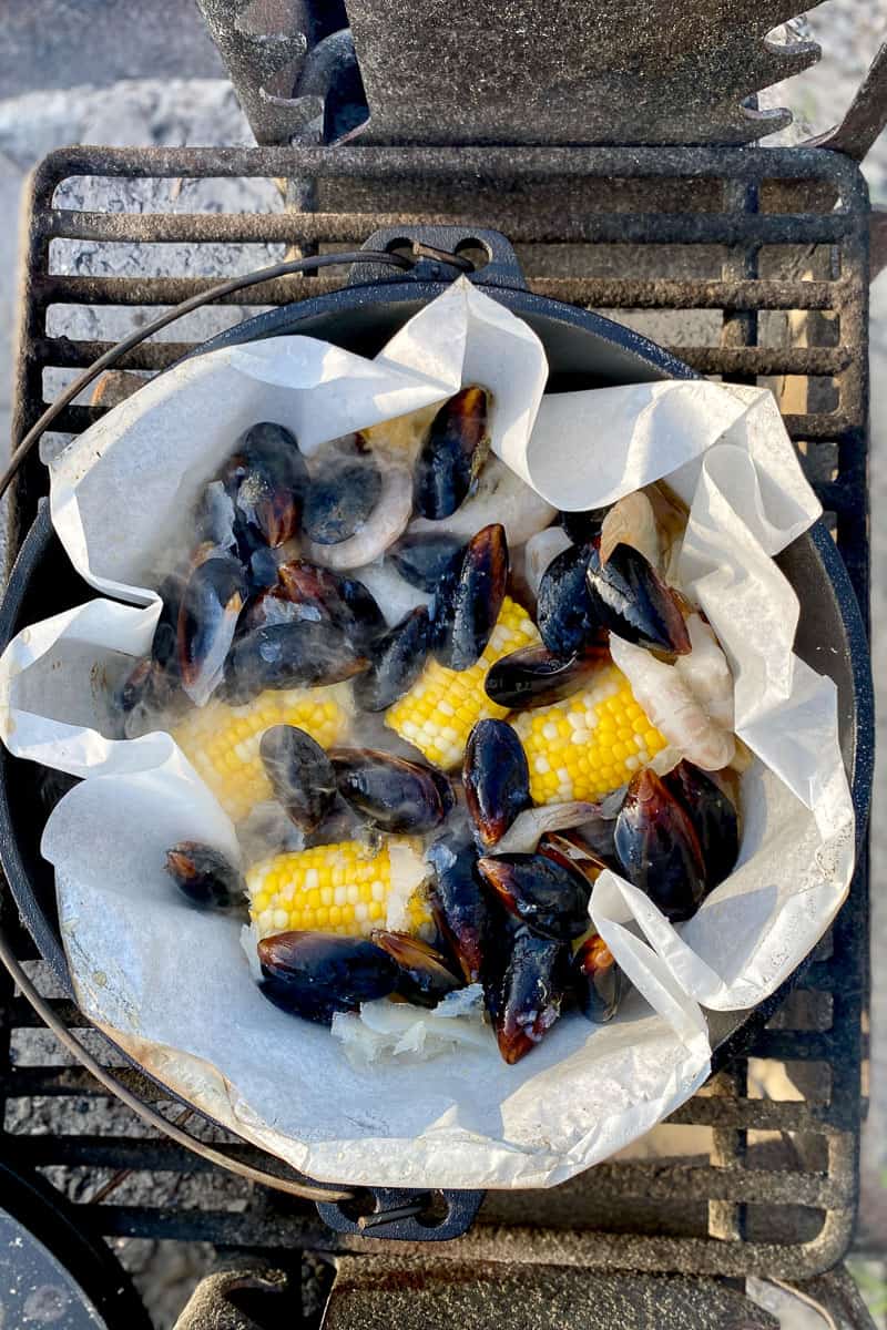 Campfire shrimp boil with corn, shrimp, mussels and butter added to potato mixture in Dutch oven.