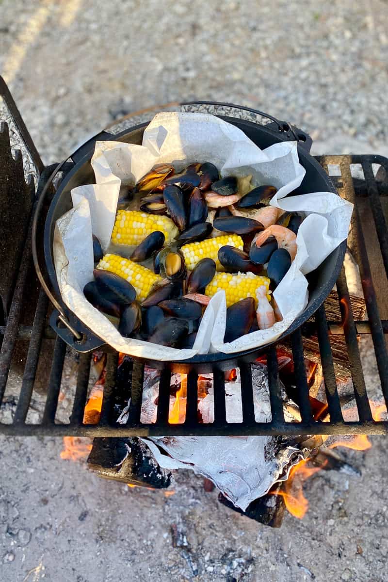 Campfire shrimp boil with mussel, shrimp, corn, and potato mixture cooked in Dutch oven.