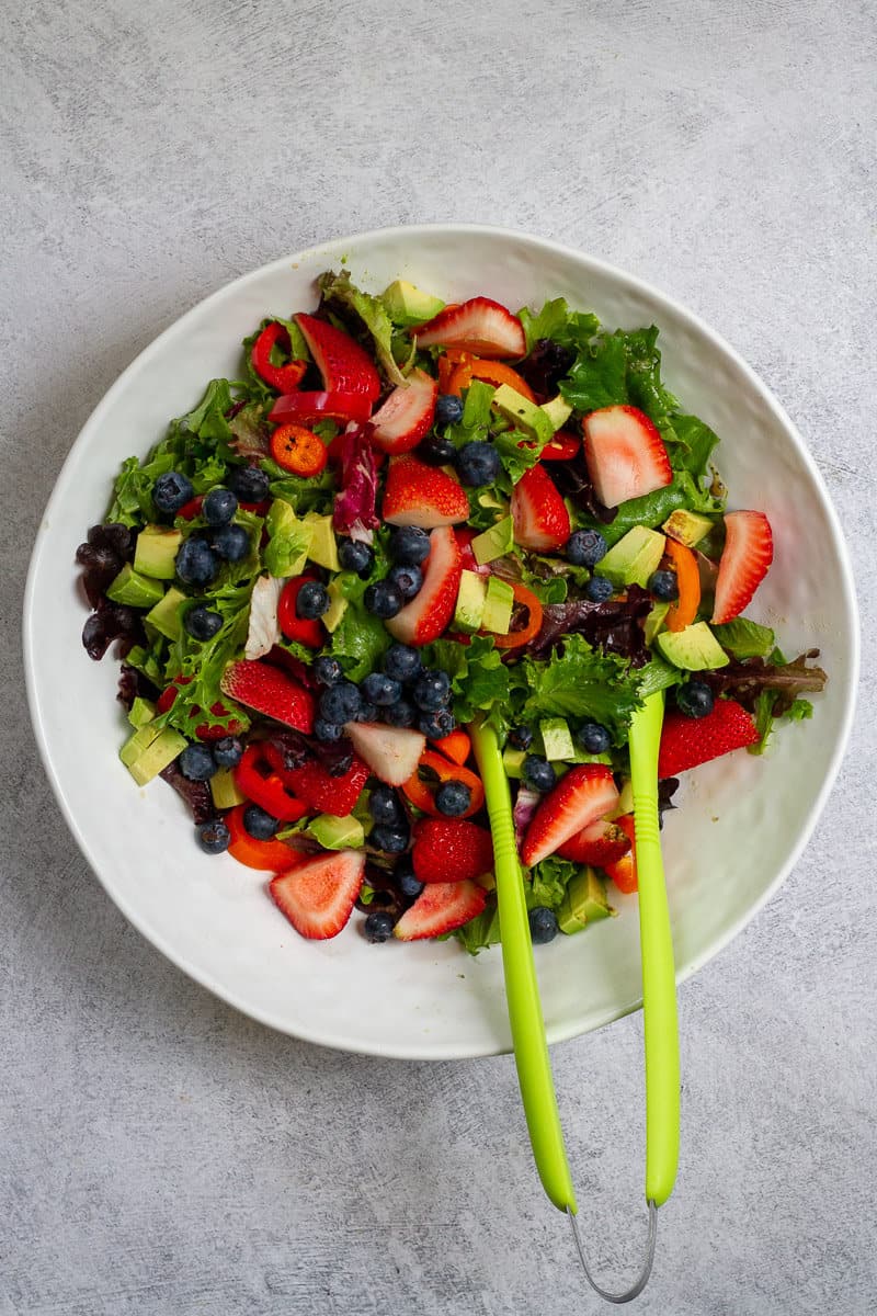 Salad with lettuce, bell peppers, avocado, fruit and seeds tossed together.