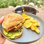 Hamburger with avocado and cheese on plate with potato chips.