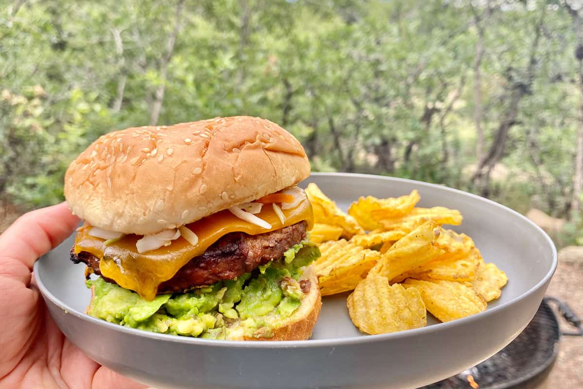 Hamburger with avocado and cheese on plate with potato chips.