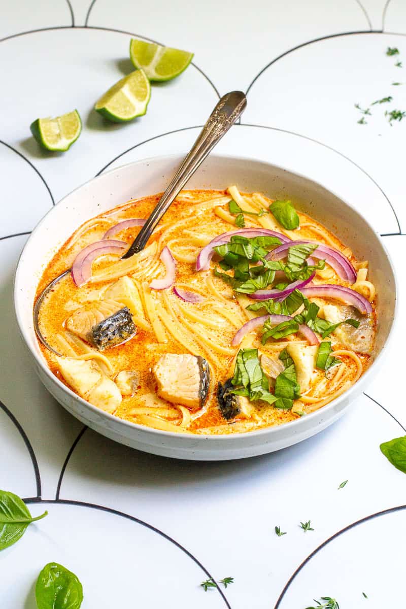 Fish coconut curry in bowl with spoon with red onions and basil sprinkled on top.