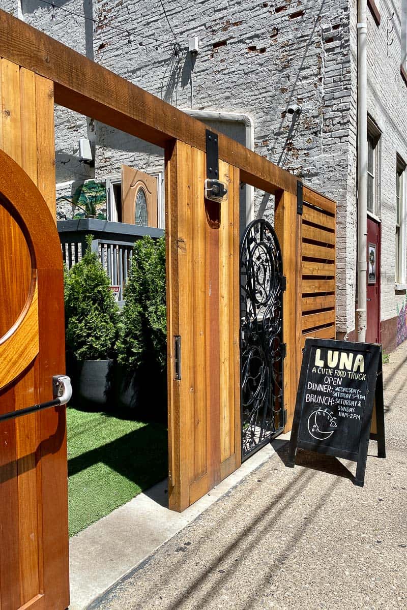 Wooden entrance gates to Luna food truck with sign board showing hours.