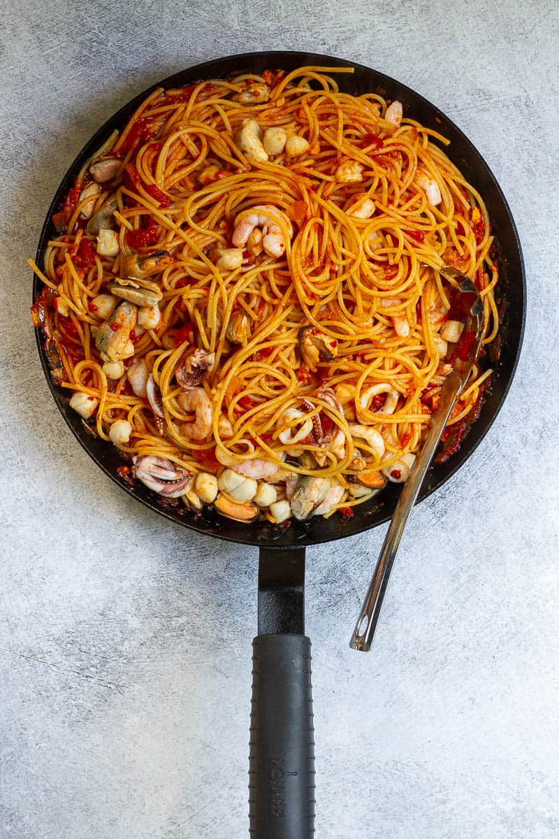 Seafood fra diavolo with pasta, seafood, and tomatoes in skillet.