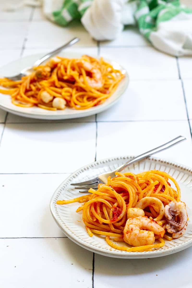 Seafood fra diavolo with pasta, seafood and tomatoes on plates with forks.