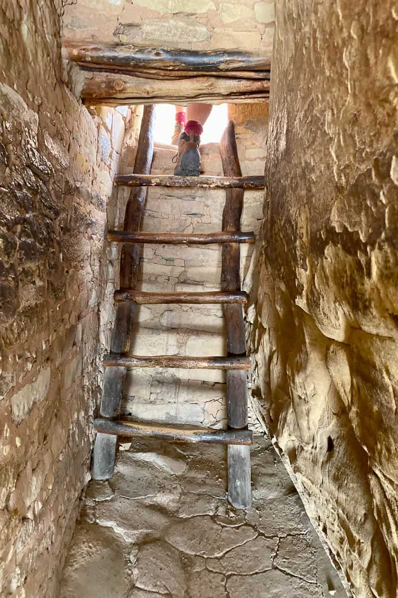 View of person's boots climbing from interior ladder to open air on Mesa Verde cliff dwelling tours.