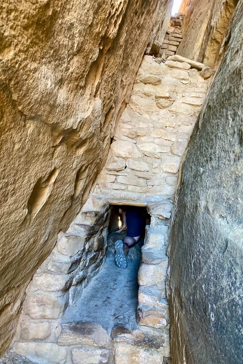 Hiker crawling through stone passageway on Mesa Verde cliff dwelling tours.