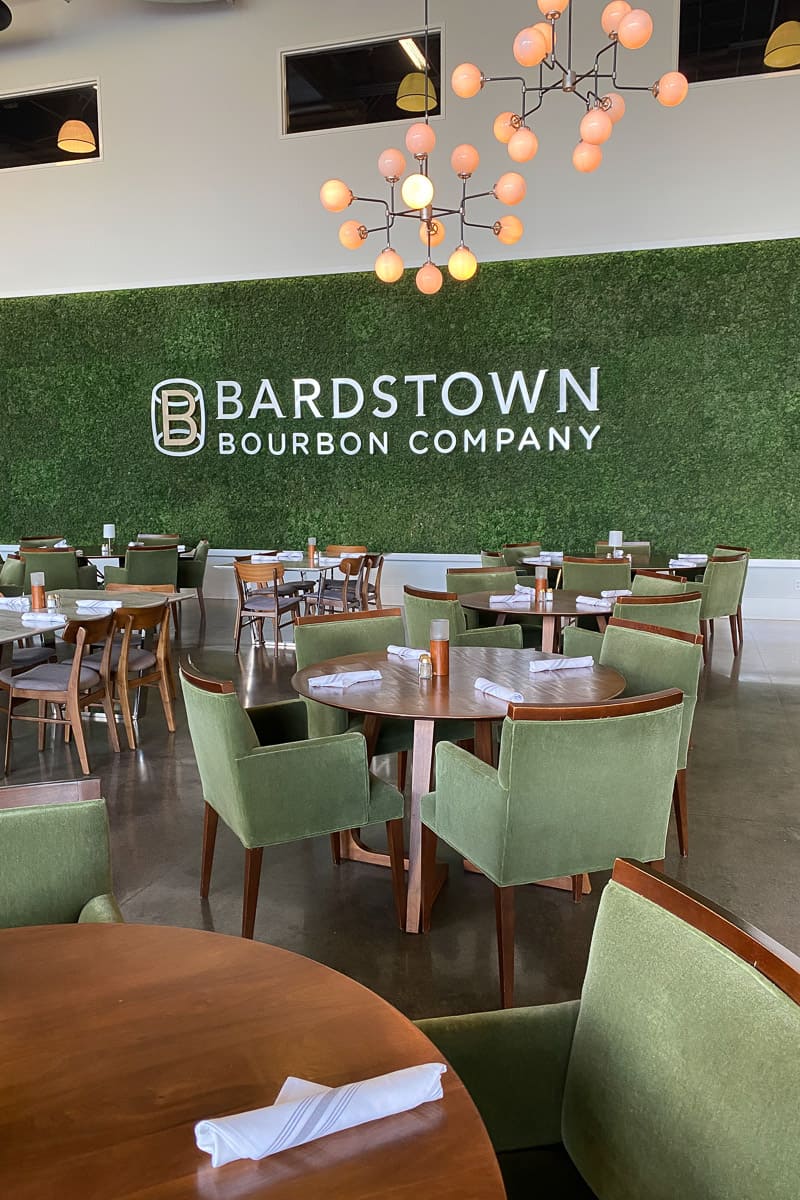 Restaurant at Bardstown Bourbon Company with tables and chairs in front of large moss-covered wall.
