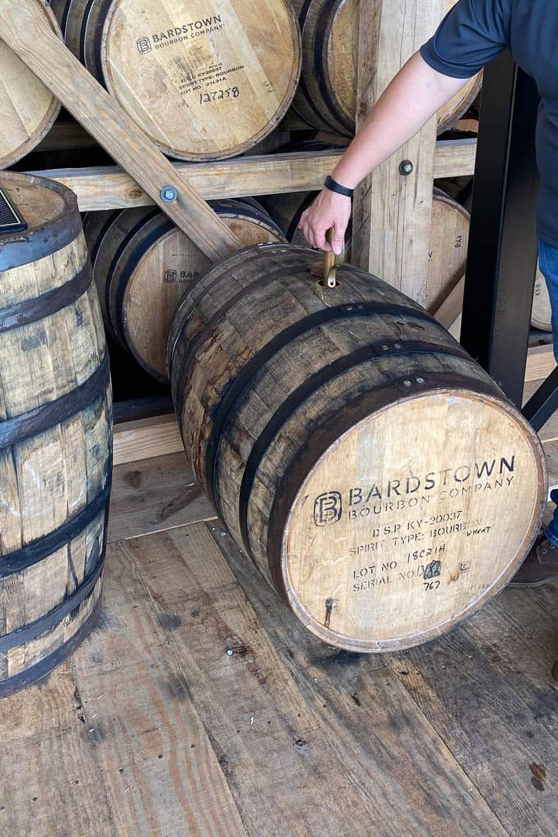 Tour guide dipping out bourbon from barrel.