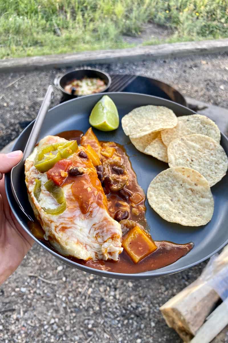 Campfire chicken enchiladas on plate with tortilla chips and wedge of lime.