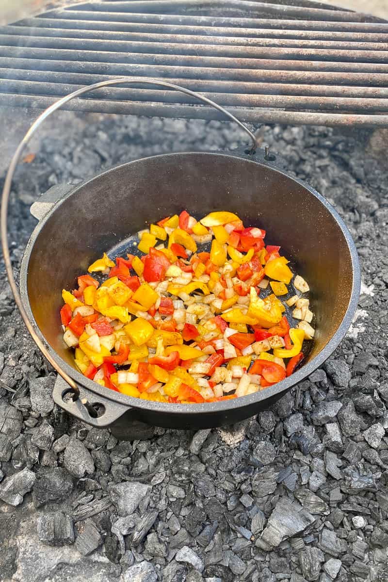 Bell peppers and onions cooking in cast-iron pan over hot coals.