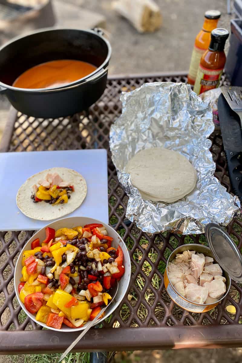 Opened can of chicken, bowl of beans, peppers, and onions, and tortillas ready to be assembled.