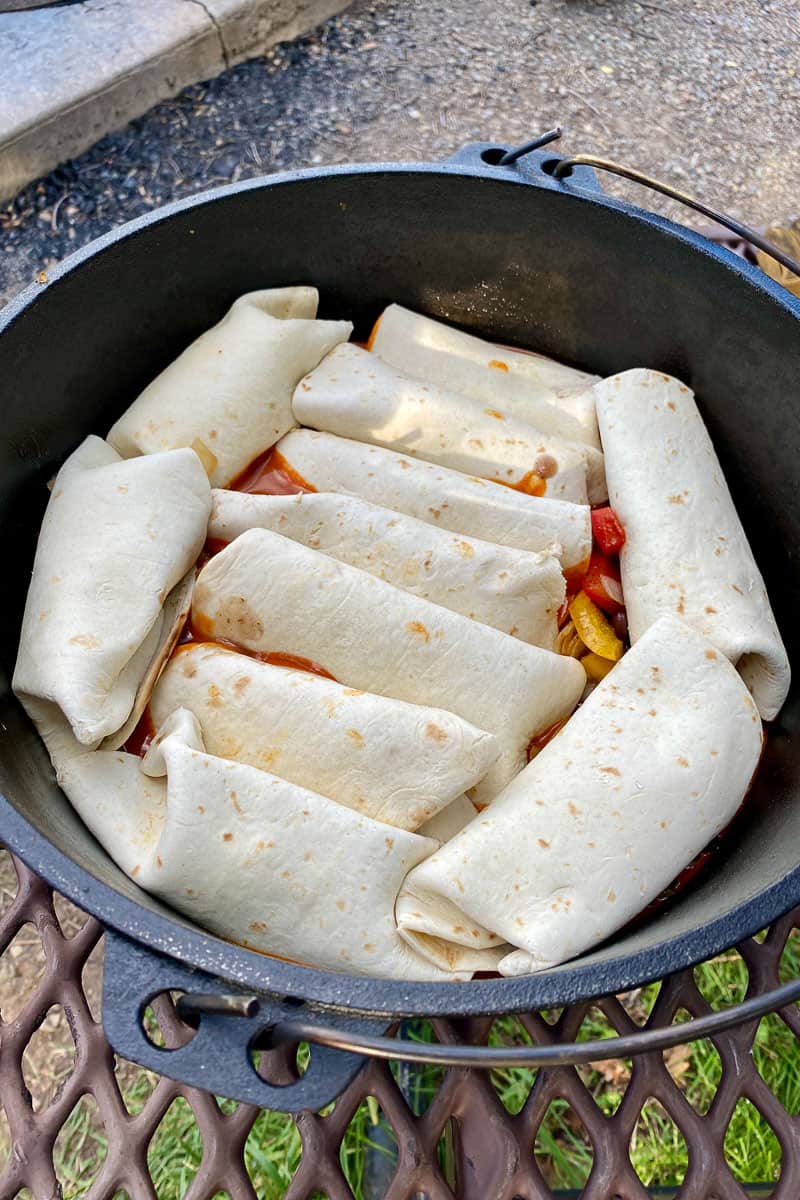 Campfire chicken enchiladas nestled in cast-iron pan for cooking.
