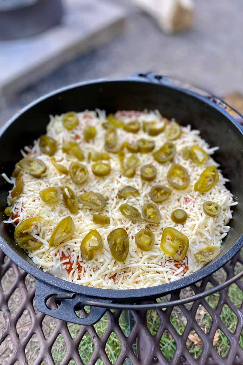 Campfire chicken enchiladas in cast-iron pan covered with shredded cheese and jalapenos.