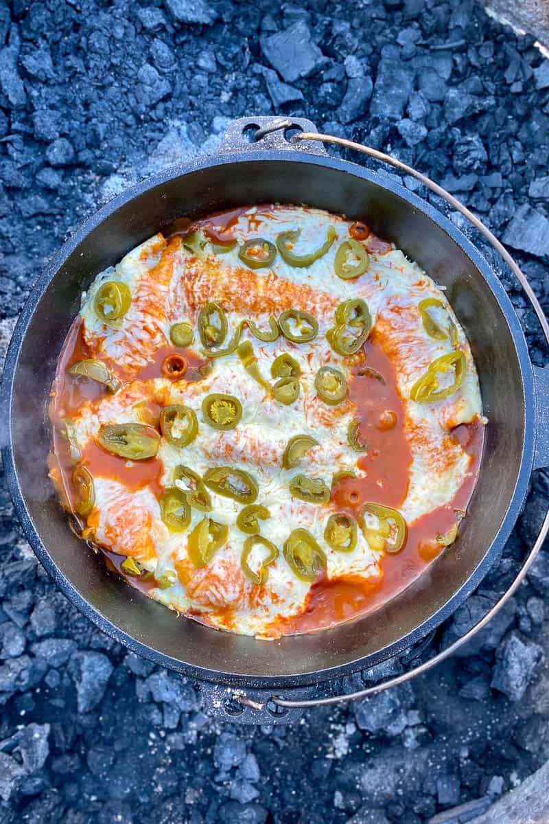 Campfire chicken enchiladas with melted cheese and jalapenos on top in cast-iron pan.