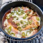 Campfire chicken enchiladas with melted cheese and jalapenos on top in cast-iron pan.