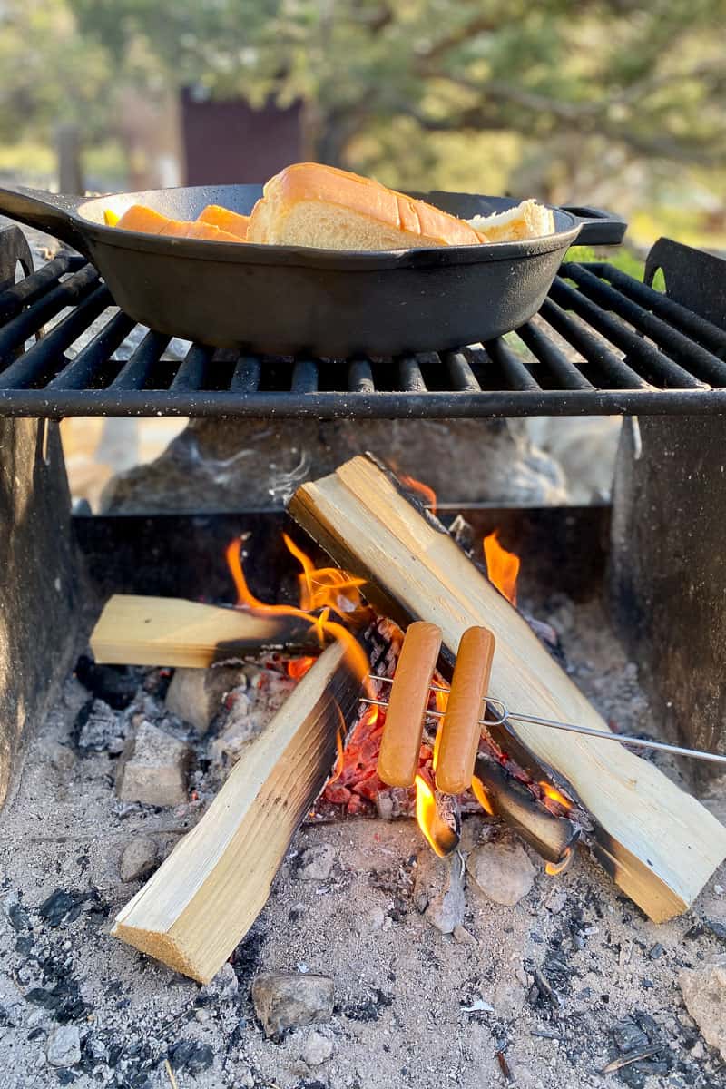 Hot dogs on a roasting stick over small campfire.
