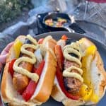 Hot dogs in buns with onions, peppers, and mustard on plate.