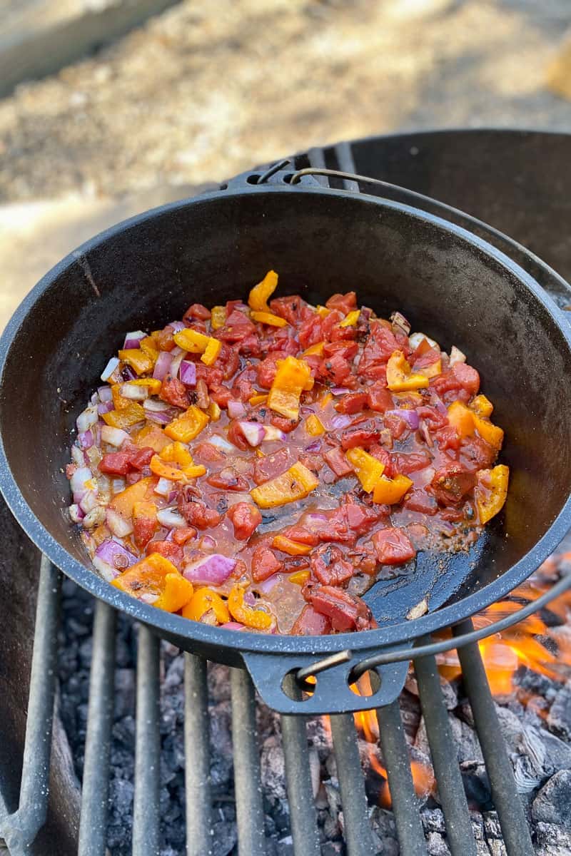 Tomatoes cooking with onions and peppers in cast-iron pan.