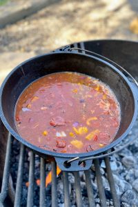 Tomatoes, peppers and onions cooking with broth and tomato sauce in cast-iron pan.