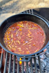 Pasta cooking with tomatoes, broth, peppers and onions in cast-iron pan.