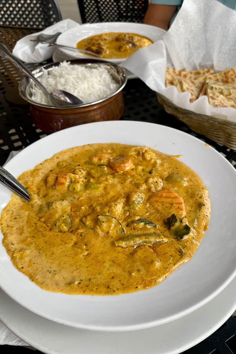 Vegetable korma with bowls of rice and bread in background.