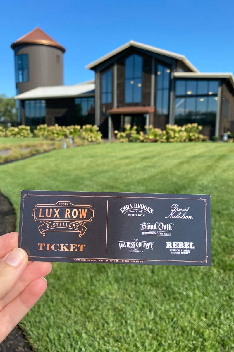 Tour ticket held in hand with Lux Row Visitor Center in background.