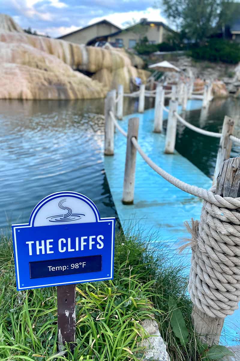Sign for The Cliffs hot springs pool next to roped walkway through water.