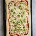 Pizza dough on baking sheet topped with tomato sauce, mozzarella, and avocado.
