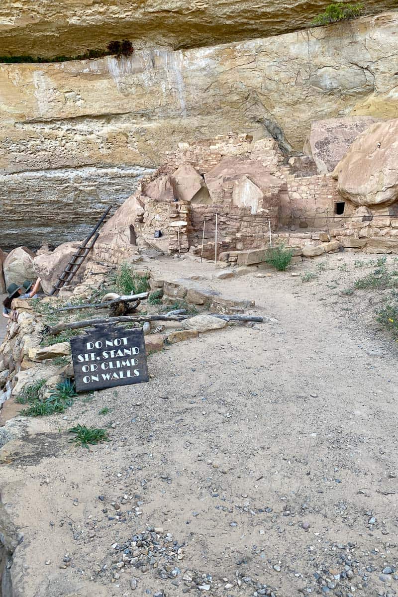 Stone houses built into cliff with sign nearby warning not to sit, stand or climb on walls.