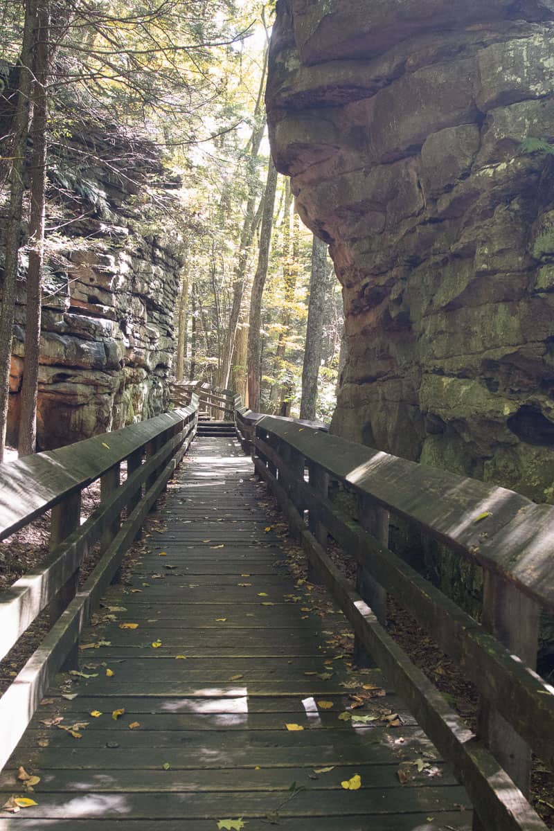 Wooden boardwalk next to rock cliff faces.