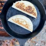 Two camping bbq chicken quesadillas in cast-iron pan over campfire.