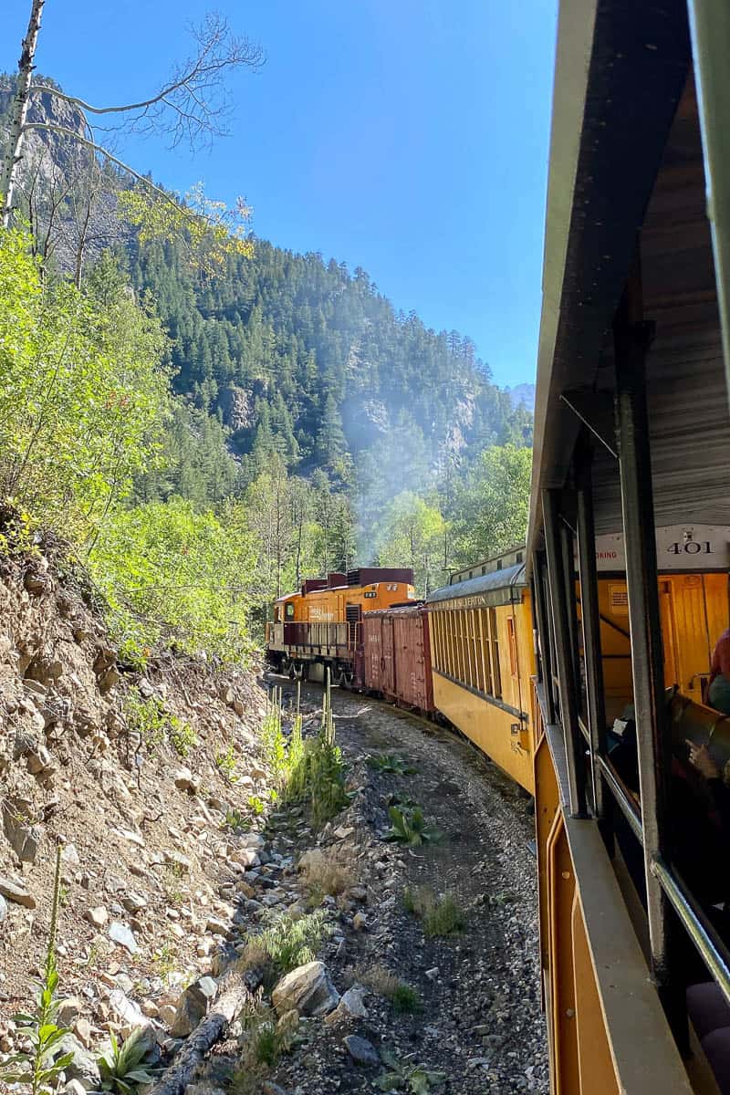 Train cars rounding a bend on the side of a mountain.