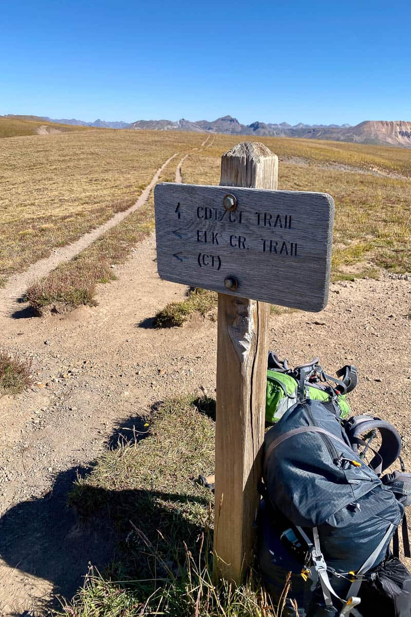 Sign pointing way to Elk Creek Trail and Continental Divide Trail with backpacks on ground, including one backpacking pack for a petite woman.