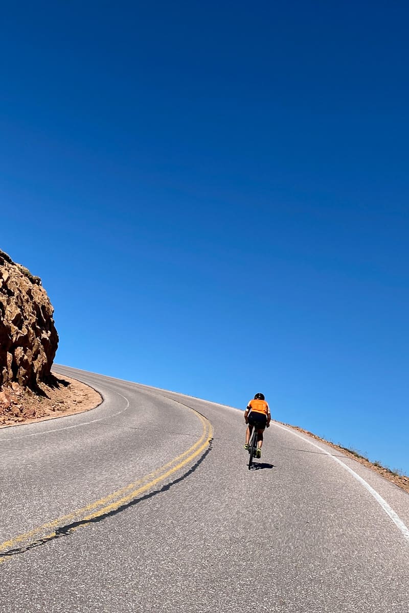 Cyclist pedaling up steep paved road.