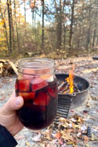 Mason jar filled with camping apple sangria with campfire in background.