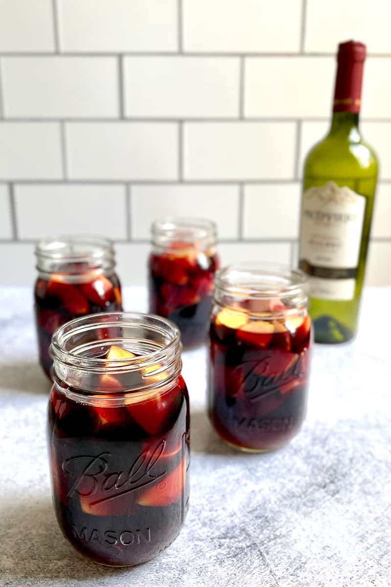 Mason jars filled with camping apple sangria with wine bottle in background.