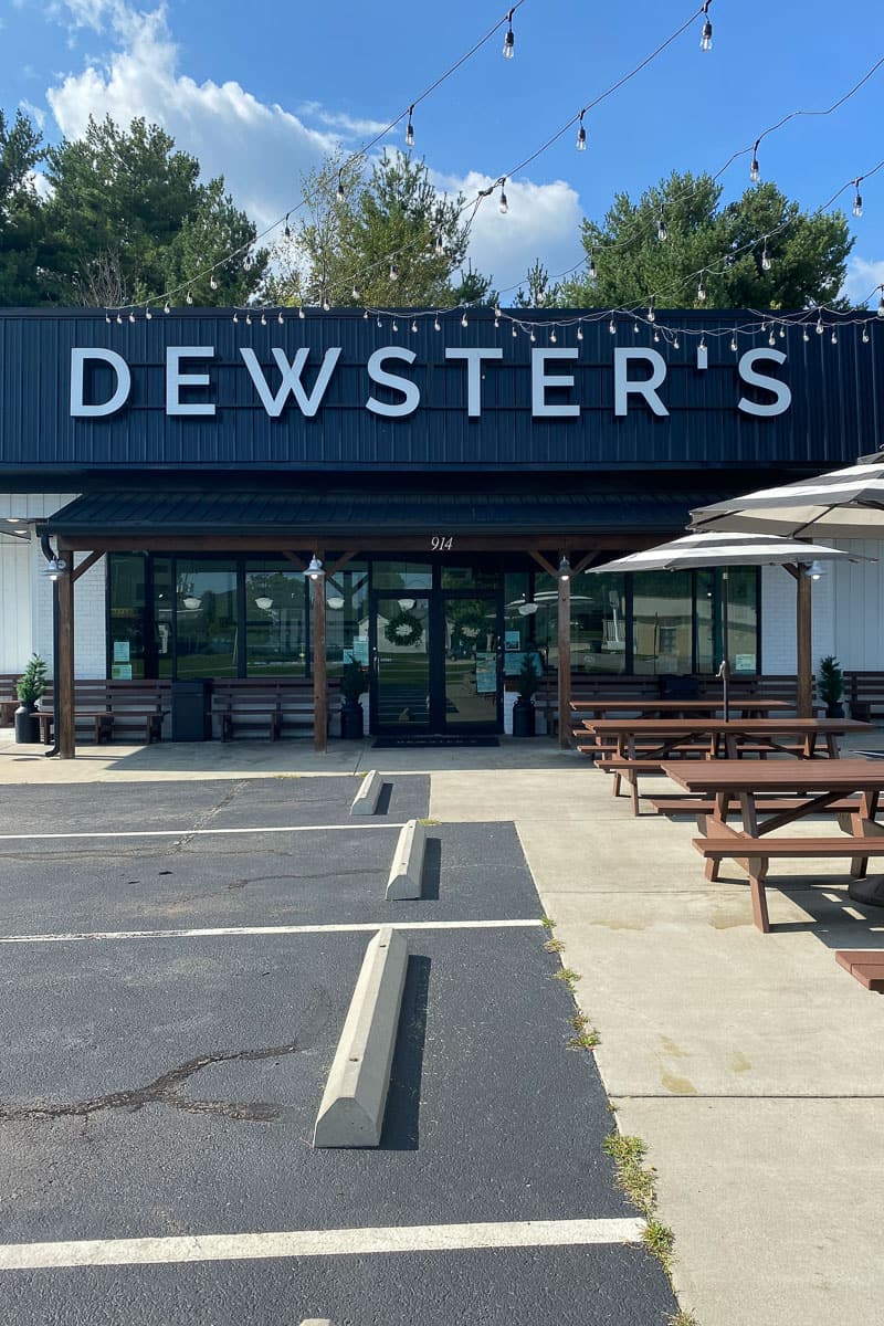 Exterior of Dewsters with picnic tables, umbrellas, and parking lot.