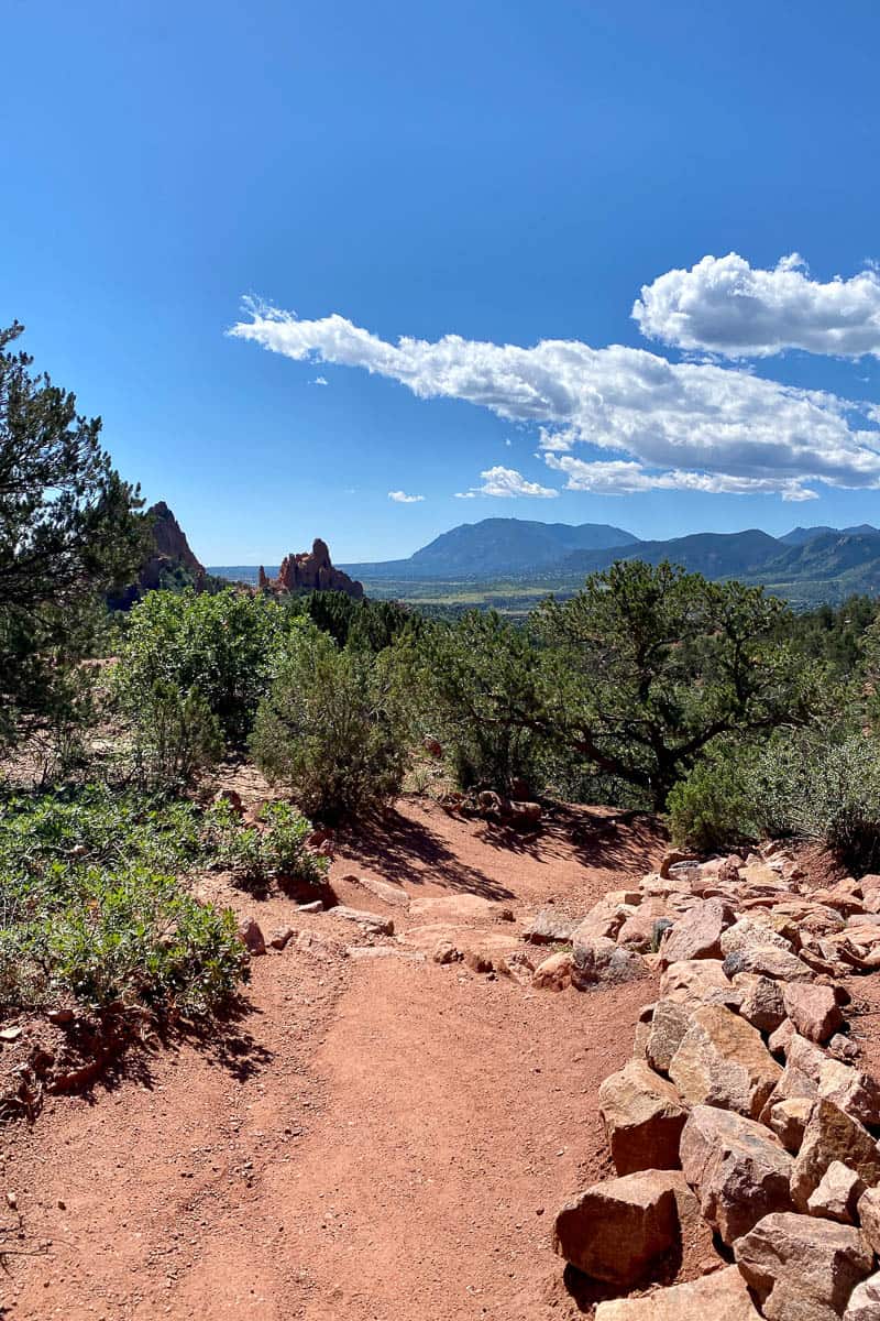 Trail bordered by red rocks with view of valley and mountain in distance.