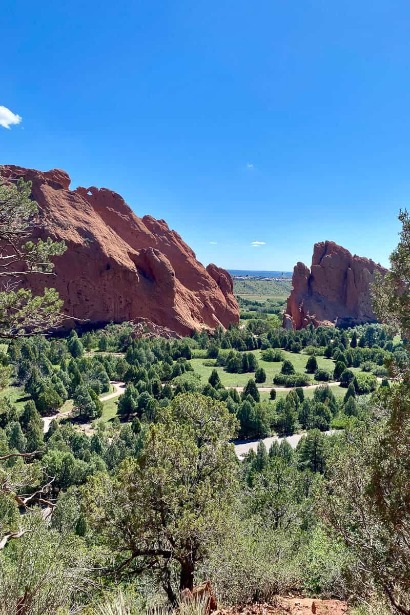 Large red rock formations towering over pathways and evergreen trees in Garden of the Gods.