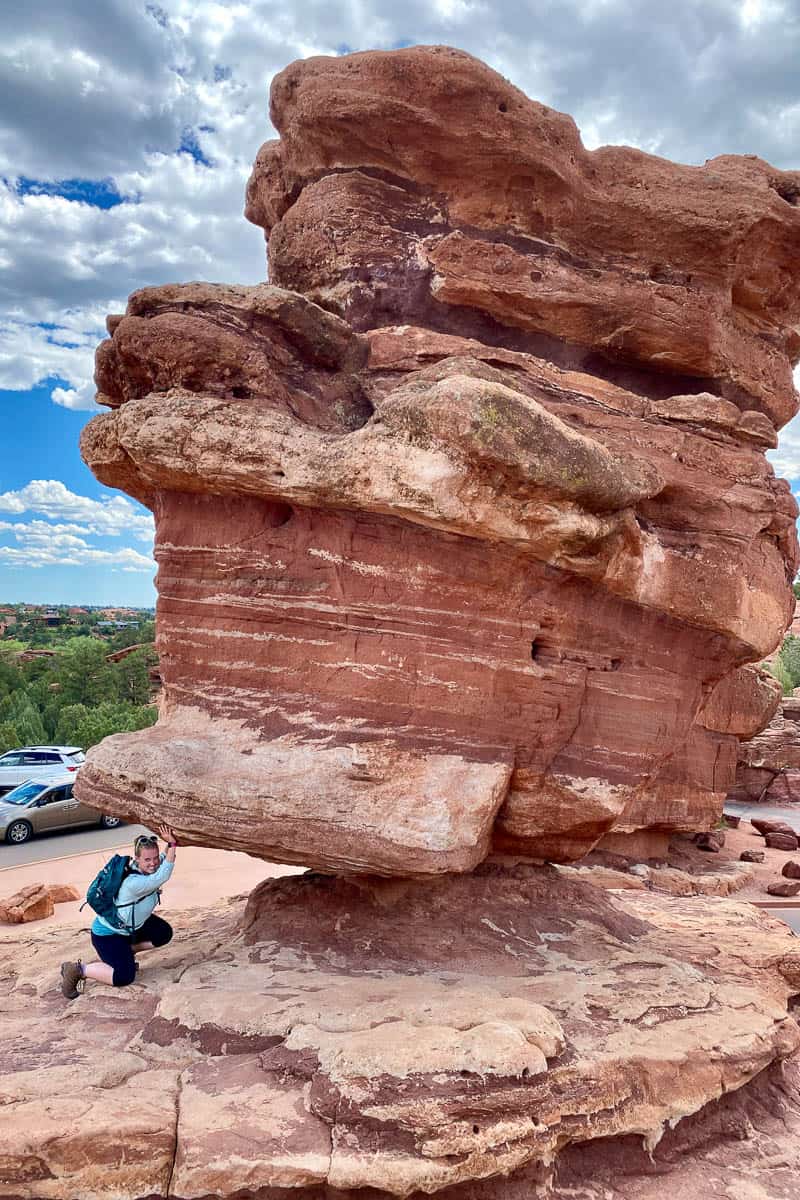 Hiker posing as if holding up large red rock formation.