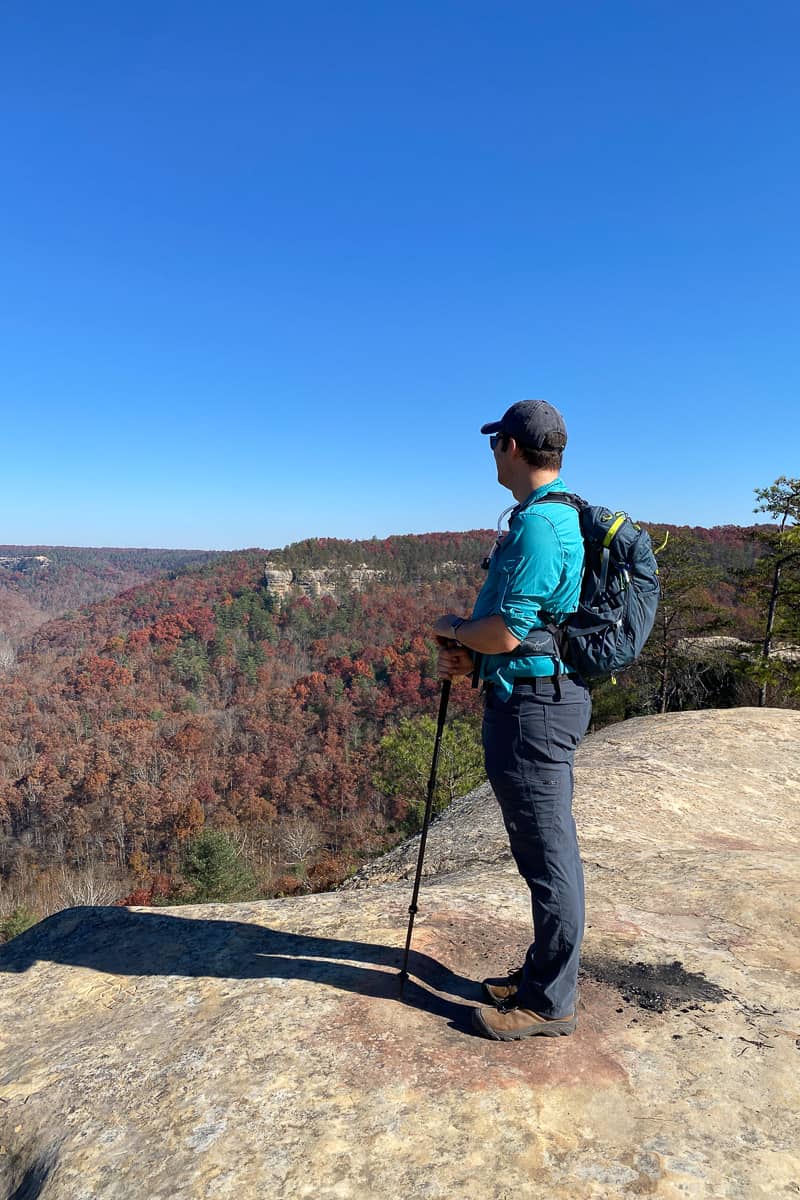 Hiker taking in the view from Hansons Point over valley of trees with red leaves.