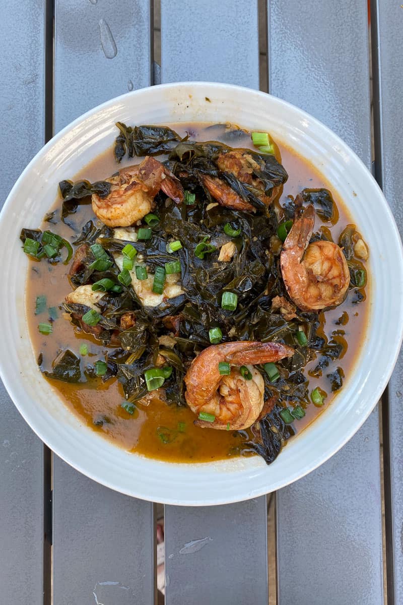 Shrimp and grits with braised greens and green onions in a bowl.