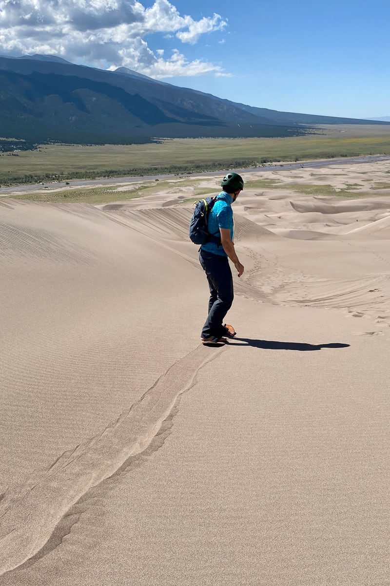 Man with backpack sandboarding in Colorado Great Dunes National Park.