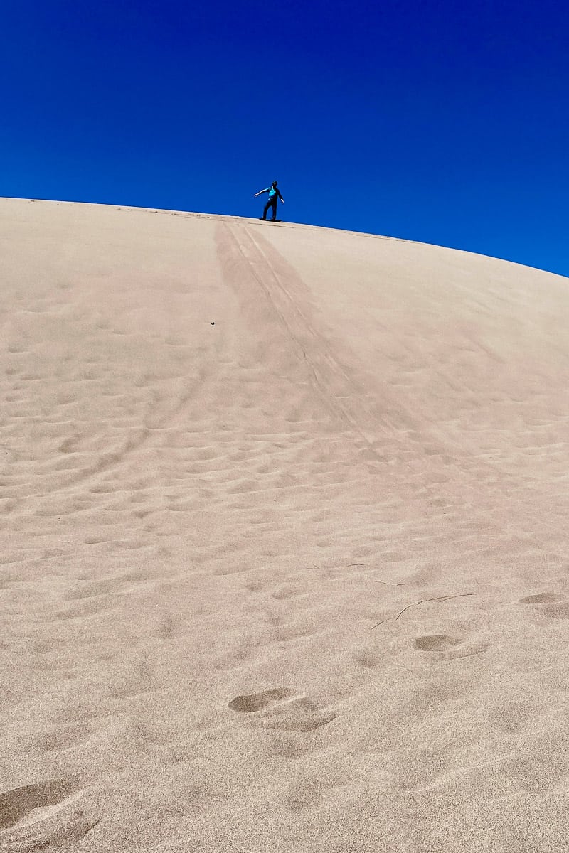 Man sandboarding in Colorado Great Sand Dunes National Park from top of dune.